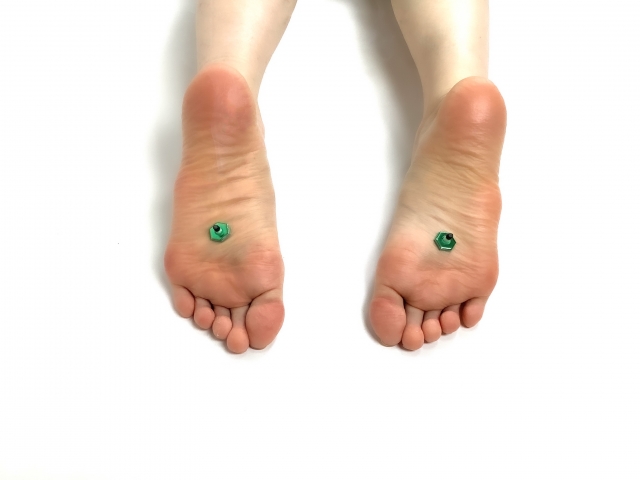 Two feet with small green gemstone tattoos or markings on the soles, displayed from above
