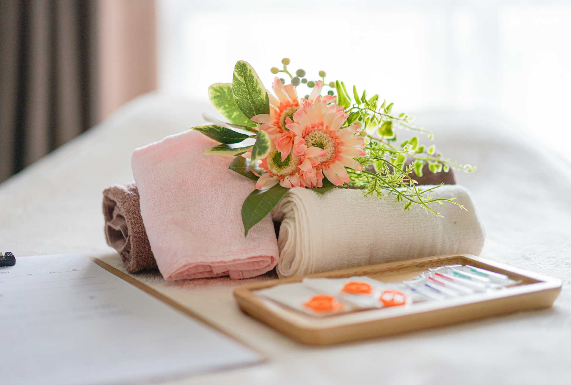 Rolled towels with coral gerbera daisies and greenery on wooden tray with color swatches