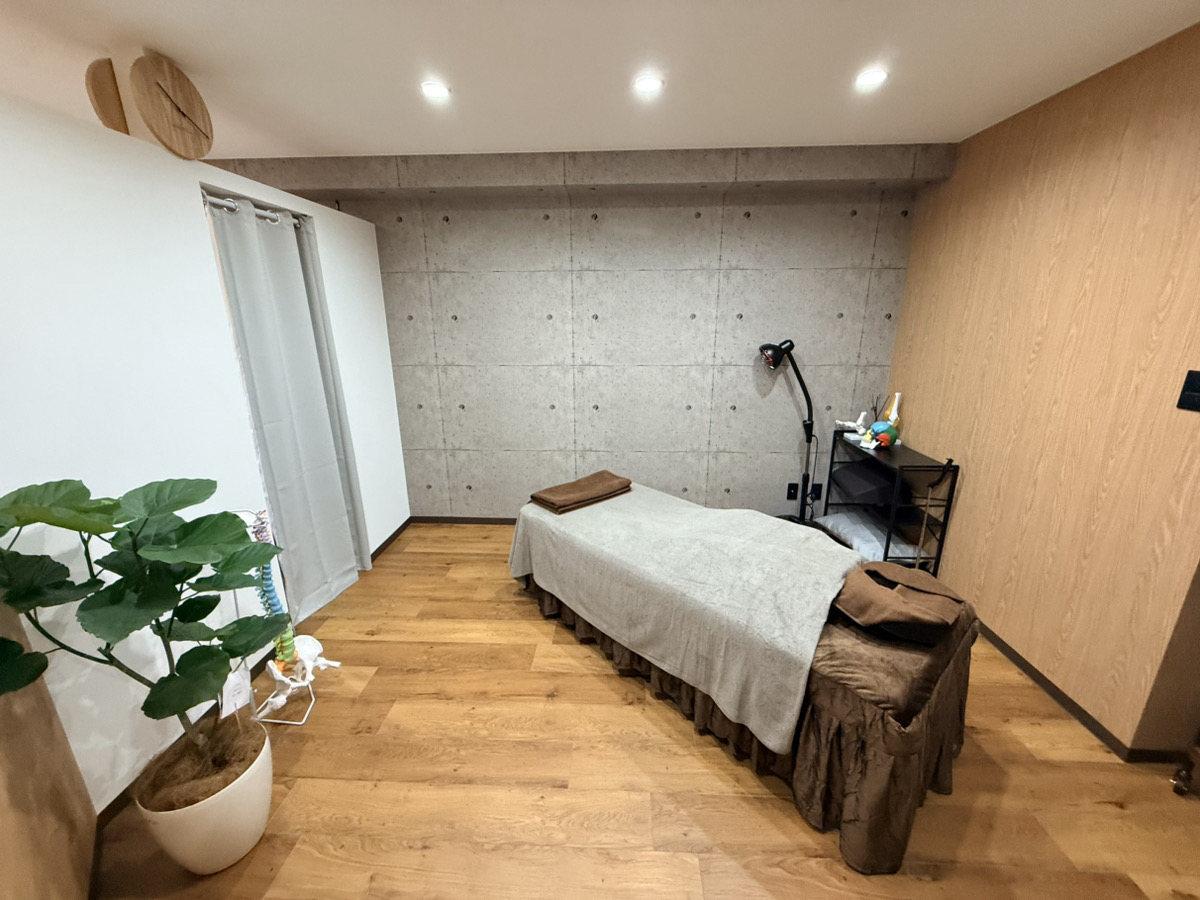 A minimalist massage or therapy room with a treatment bed, concrete wall, and wooden flooring