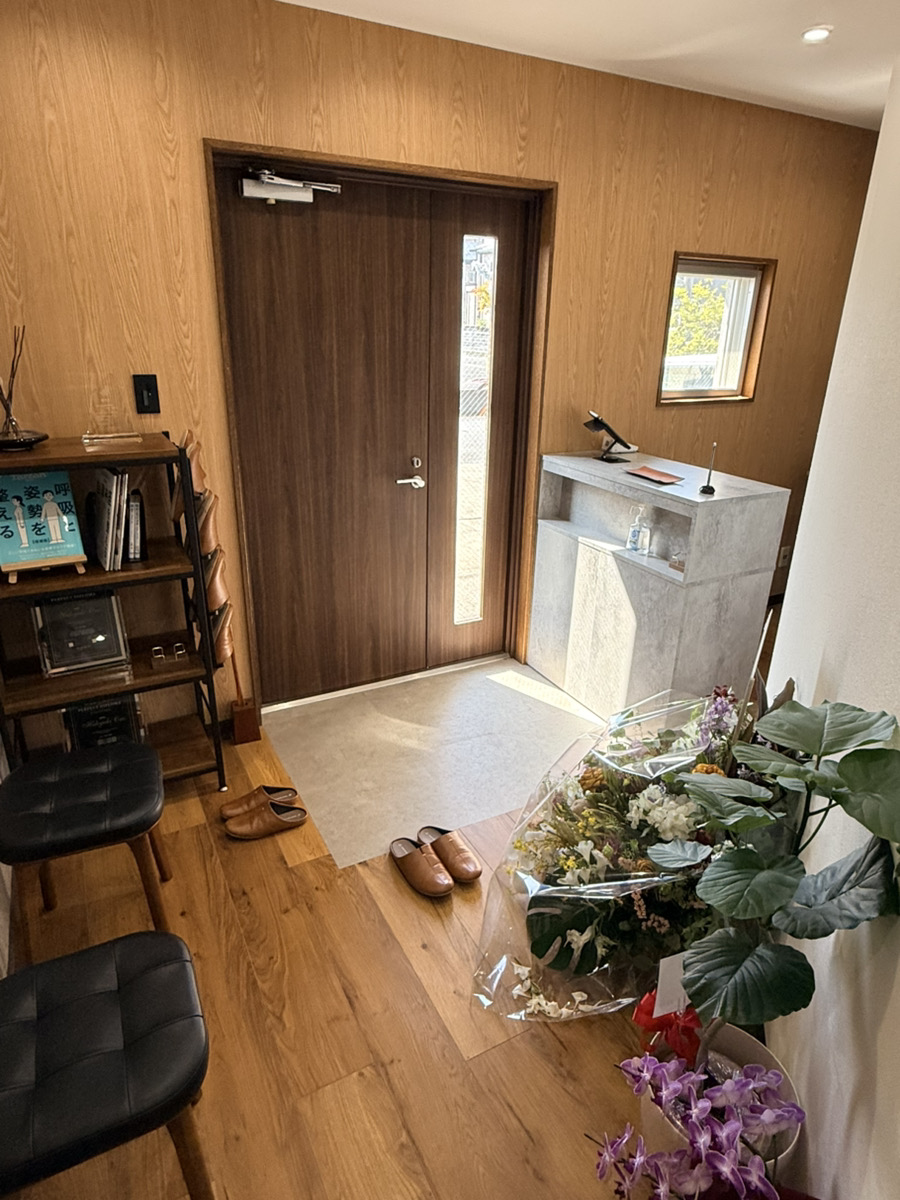 Modern entryway with wooden walls, reception desk, shelving unit, and potted flowers