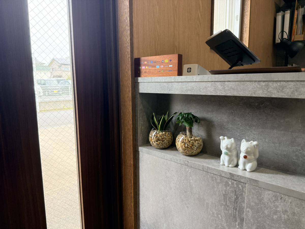 Modern shelving unit with potted plants, white decorative figurines, and electronics against wood paneling