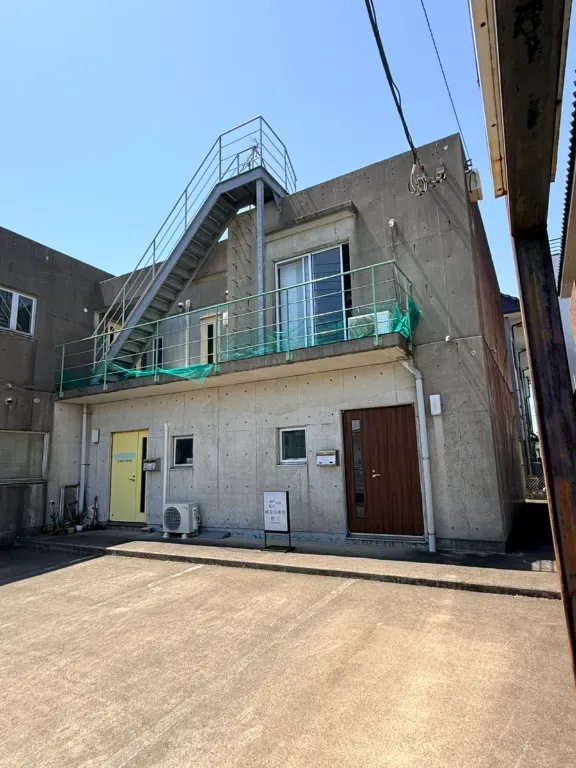 Modern concrete building with upper deck, stairs, and green railings on sunny day